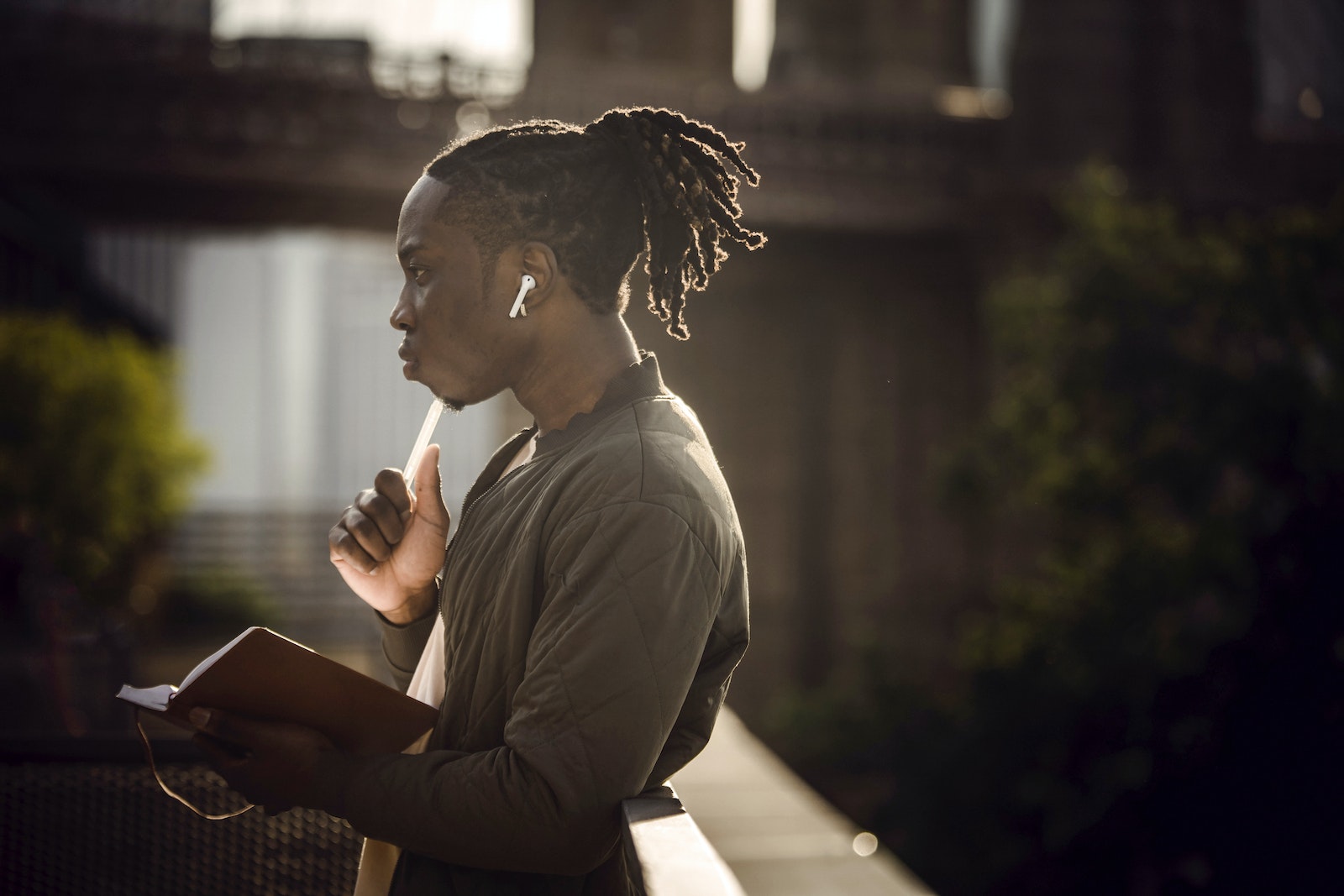Young thoughtful black male student with notebook in city park