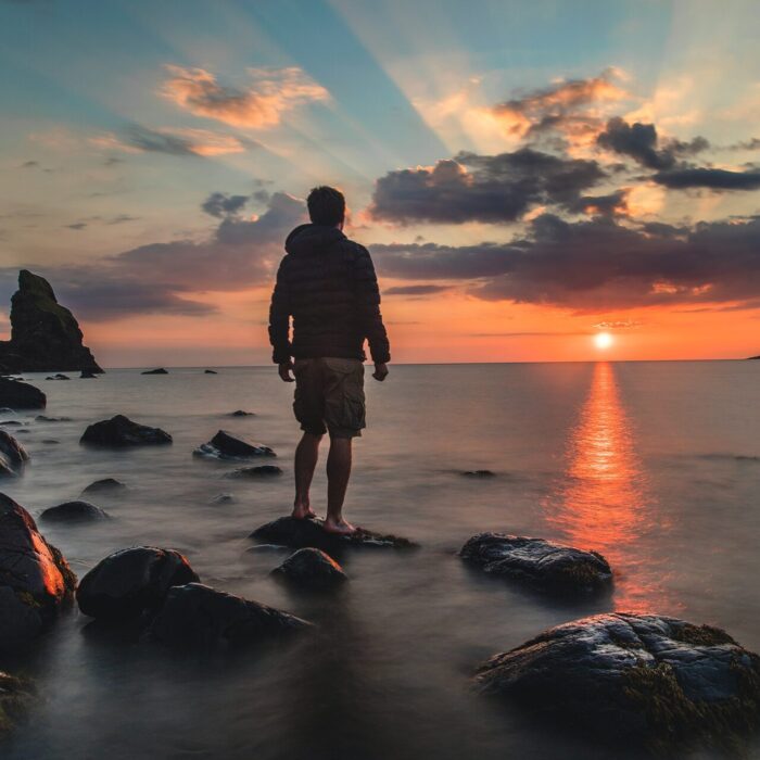 man standing on stone looking at sunset